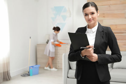 woman with folder in foreground and woman cleaning area in background