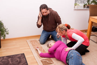 one person on phone while another person tends to an unconscious person
